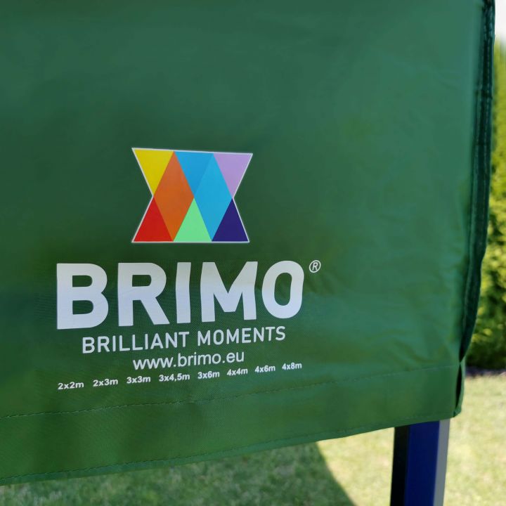 Detalj av det gröna tyget (tak/sidor) på tältet med den vita logotypen "BRIMO" och färgglada trianglar.